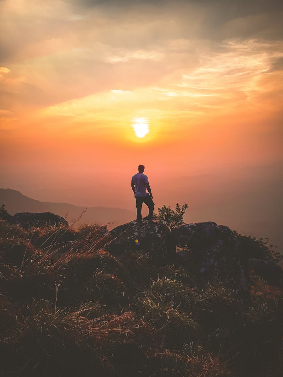 A lone hiker admires a stunning sunset view from Ponmudi Peak, creating a serene landscape scene.